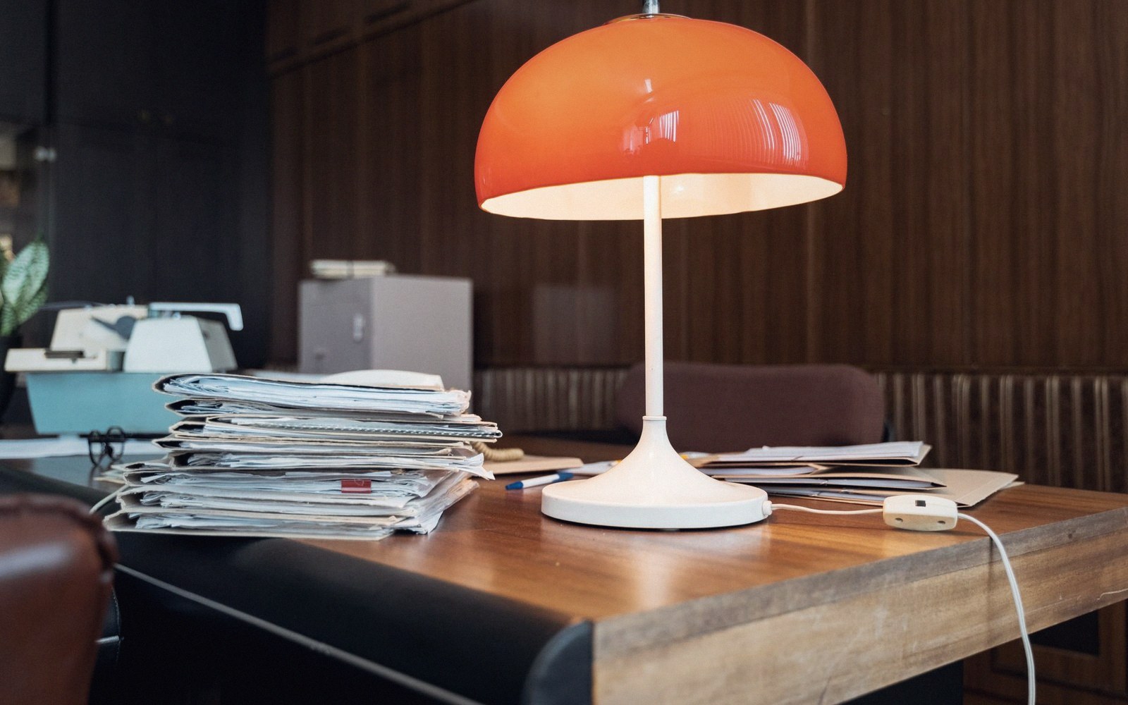 A plain desk with a lamp and a stack of reports